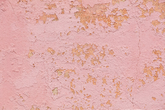 A pink wall with a lot of cracks and peeling paint