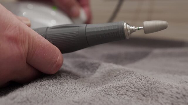 A hand holds the plastic and metal rotary handpiece of an electric nail drill as the rotation speed is adjusted. The spinning action causes the pitch of the electronic buzzing sound
