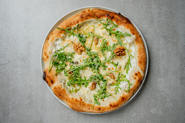 Freshly baked pizza adorned with arugula and walnuts served on a sleek gray surface