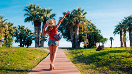 Happy woman on wooden path or paseo toward sea with coconut abnd palm. Summer travel destination, relaxing vacation