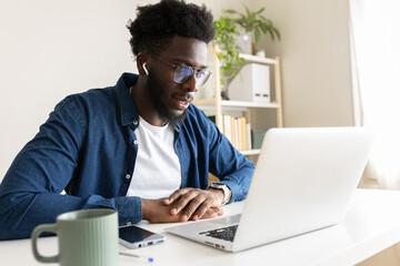 African american man looking at laptop screen during video call at home office.