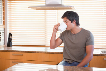 Adult male sitting at kitchen counter drinking from white mug on stone countertop, copy space