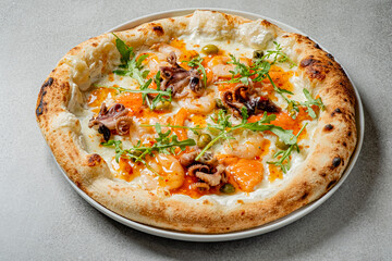 Seafood pizza topped with shrimp, octopus, and arugula sits on a light gray table, ready to enjoy
