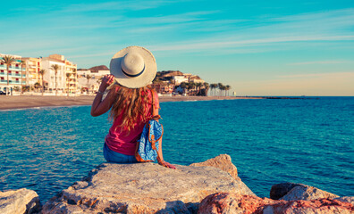 A woman sitting on rock, looking at typical village in Coasta Tropical, Andalousia, Torrenueva in province de Granada. Travel destination in Spain