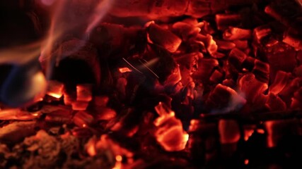 Red hot charcoal embers glowing and burning with flames licking across them. A slow motion detail of a fireplace or barbecue grill - Powered by Adobe