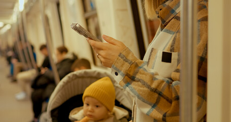 Young woman using her smartphone while commuting on a subway train with her baby in a stroller