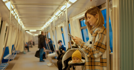 Woman multitasking, using smartphone while pushing baby stroller inside busy subway carriage, embodying digital parenting lifestyle