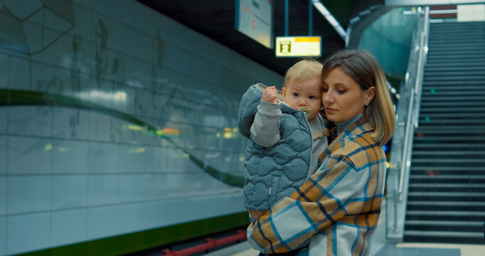 Caring young mother tenderly holding infant while waiting on subway platform during daily urban commute, embodying family connection and metropolitan life