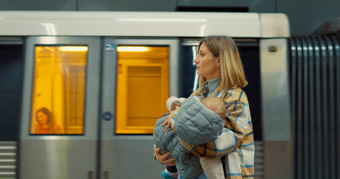Mother lovingly embracing sleeping baby in arms while waiting on subway station platform, representing urban family commute and maternal connection
