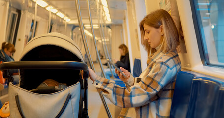 Subway car interior with young mother using her smartphone while traveling with a baby stroller
