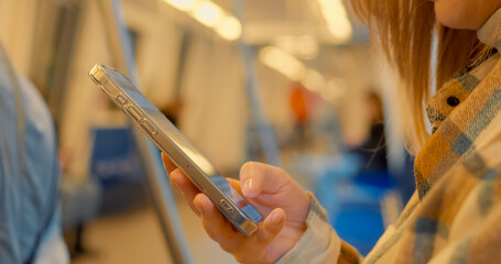 Woman intently engaging with smartphone while commuting through subway train, navigating digital connectivity during urban travel