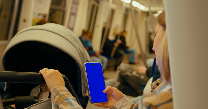 Woman using smartphone with chroma key blue screen while commuting on subway train next to baby stroller - Powered by Adobe