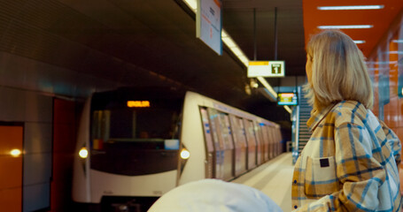 Female waiting for subway train while using her smartphone and holding a stroller on platform
