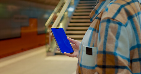 Woman commuting through urban subway, holding smartphone with blue screen, representing modern digital connectivity and mobile communication lifestyle