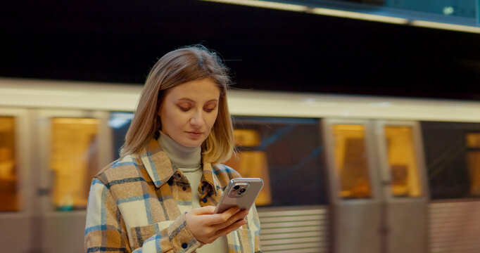 Woman engaging with smartphone while waiting for train, embodying urban digital communication lifestyle - Powered by Adobe