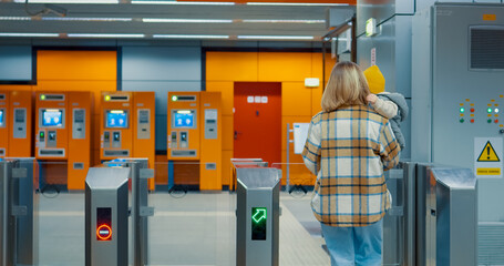 Young mother carrying her baby walks through an automatic turnstile in a modern subway station