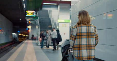 Caring young mother waiting patiently with baby stroller on subway platform, representing urban family life and daily commute