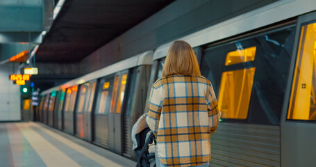 Young mother standing near subway platform, waiting with stroller while watching digital clock during daily commute in metropolitan station