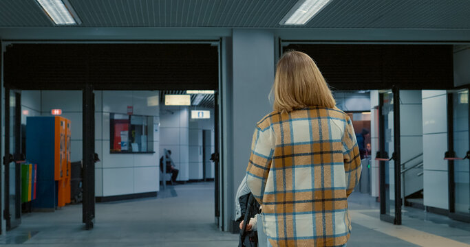 Young parent navigating empty subway platform, pushing stroller through minimalist urban corridor with contemporary architectural design