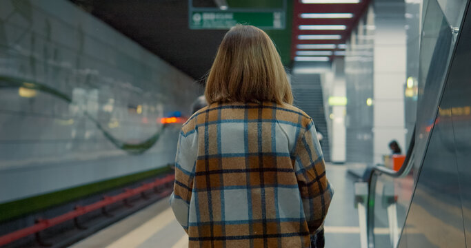 Young mother waiting patiently on subway platform, standing near baby stroller while navigating urban commute with infant - Powered by Adobe