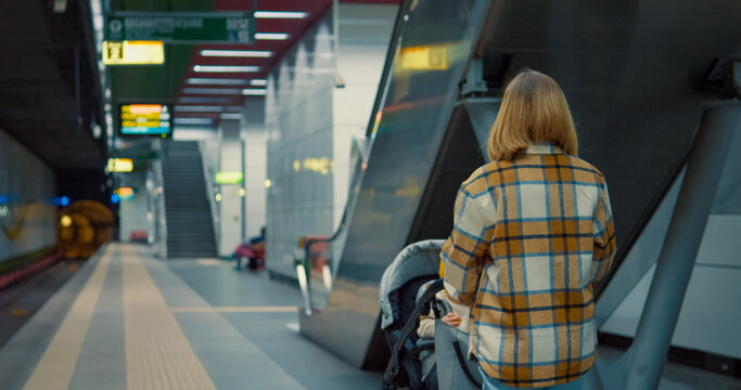Mother waiting on subway platform, holding baby stroller while anticipating train arrival in urban transit environment