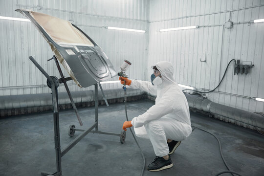A technician spray-painting car hood inside a controlled automotive spray booth
