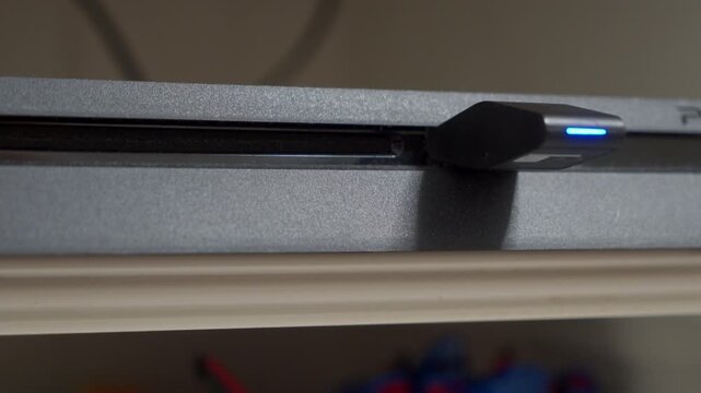 A black plastic gaming console is running, with a Bluetooth USB dongle inserted, showing a blue connection light. The console's internal fan is operating, producing a steady, low humming fan noise.