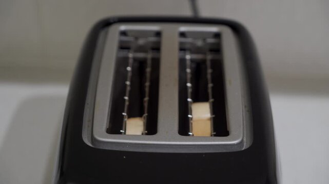 A two-slice plastic and metal toaster is shown with two slices of bread inserted into the slots, falling down to the heating elements.