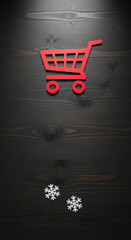 Red shopping cart cutout and snowflakes on dark wood background, idea of winter holiday sale, promotion for Christmas or Black Friday.