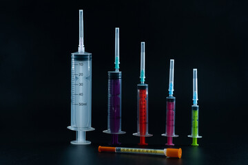 A composition of various size syringes on a dark background, highlighting themes of measurement, vaccination, and lab work.