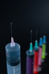Sharp Focus on Syringe Needle Tip with Fluid Drop. A composition of various size syringes on a dark background, highlighting themes of measurement, vaccination, and lab work.