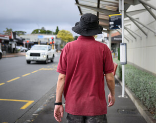 Senior man walking towards bus stop. Bus timetable on the post. Auckland.