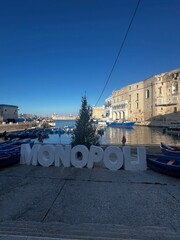 Fototapeta premium Monopoli harbor view: Capturing the unique harbor view with the city name as the focal point, embracing the atmosphere of a beautiful day under the blue sky. 