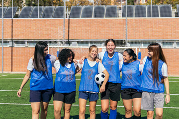 Young female soccer players standing on a pitch, smiling and embracing, showing teamwork and sportsmanship