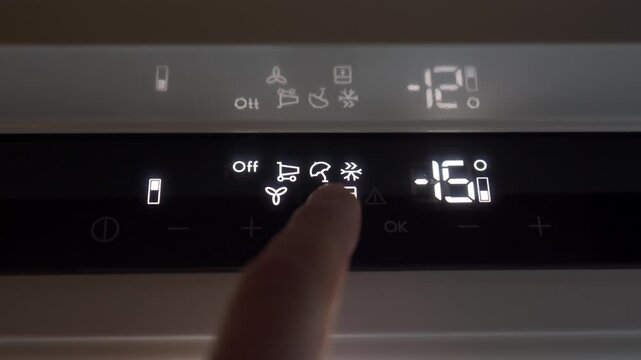A finger presses a button on the illuminated electronic touch panel of a refrigerator's control display. The selection action produces a soft, electronic click sound.