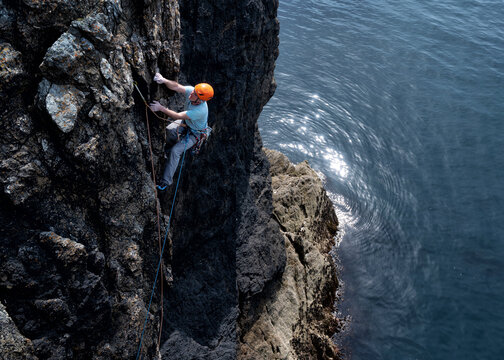 Climber ascends sea cliff with helmet and safety rope in Wales