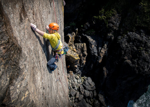 Climber scaling steep cliff face outdoors in Cornwall UK