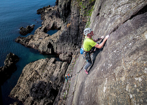 Climber ascending coastal rock face with safety gear in Pembrokeshire Wales