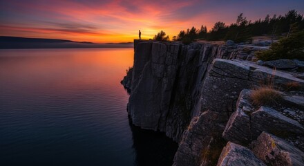 Cliffside Silhouette Captures Sunsets Fiery Embrace Over Serene Waters.