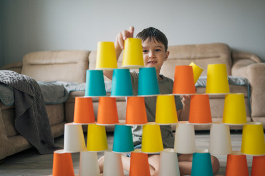Child playing game and building colorful pyramid with paper cups indoors