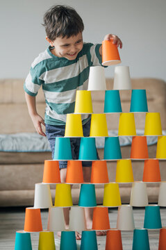 Smiling child playing and building colorful paper cup pyramid indoors