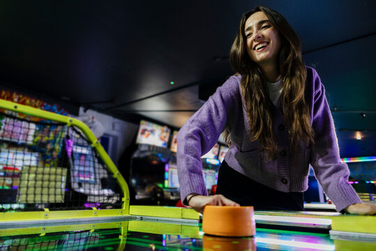 Smiling woman playing air hockey in arcade at night