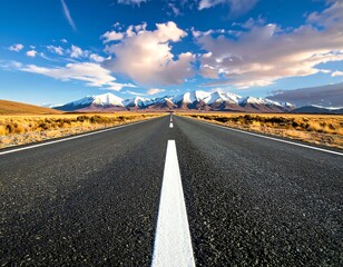 Endless road leads to majestic snow-capped mountains under blue sky.