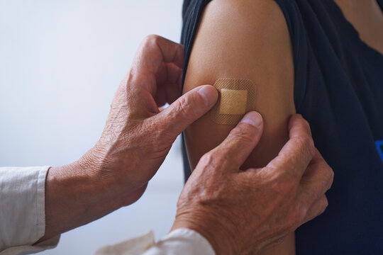 Doctor applying adhesive bandage on arm after vaccination at hospital - Powered by Adobe