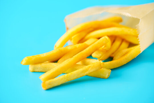 French fries on blue background in paper bag representing fast food