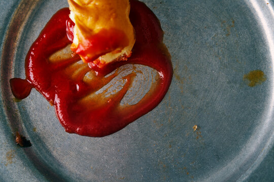 Smudged ketchup and leftover food on a dirty dish close up