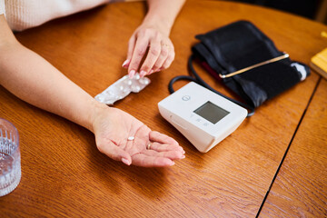 Hand holding pill next to blood pressure monitor for healthcare at home