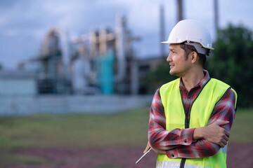 Engineer standing confidently at industrial site, wearing safety vest and helmet, symbolizing professionalism and responsibility in industrial operations.