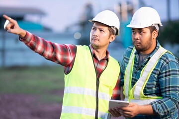 Two engineers wearing safety helmets reviewing real-time data on tablet under evening light, representing efficiency and digital innovation in modern industry.