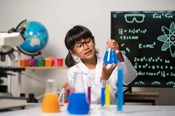 Girl in white lab coat holding chemical flask and smiling in science classroom, representing curiosity, confidence, and innovation in education.